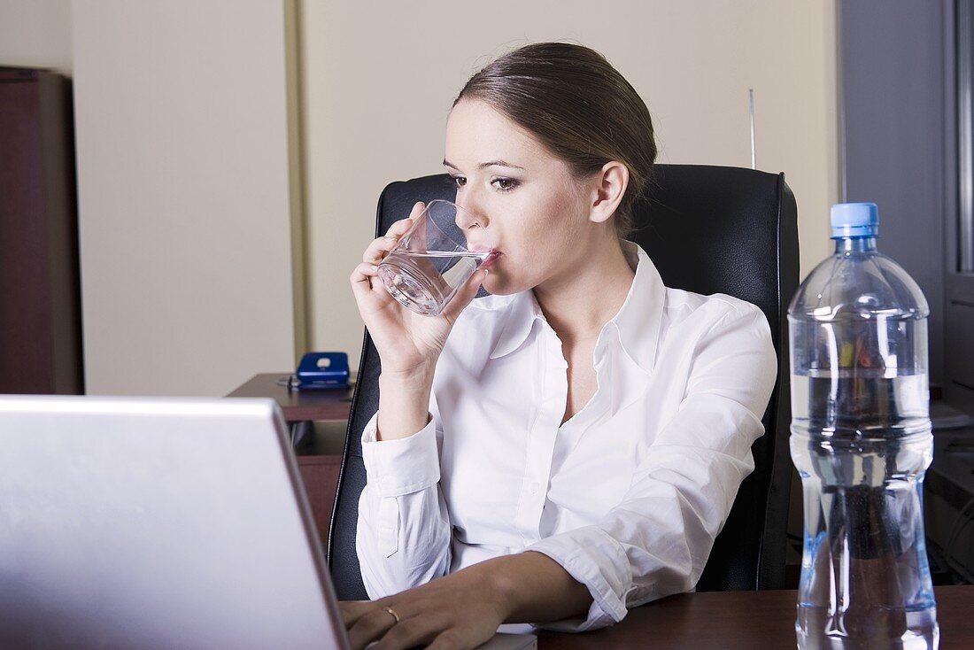 Junge Frau sitzt am Computer und trinkt Wasser