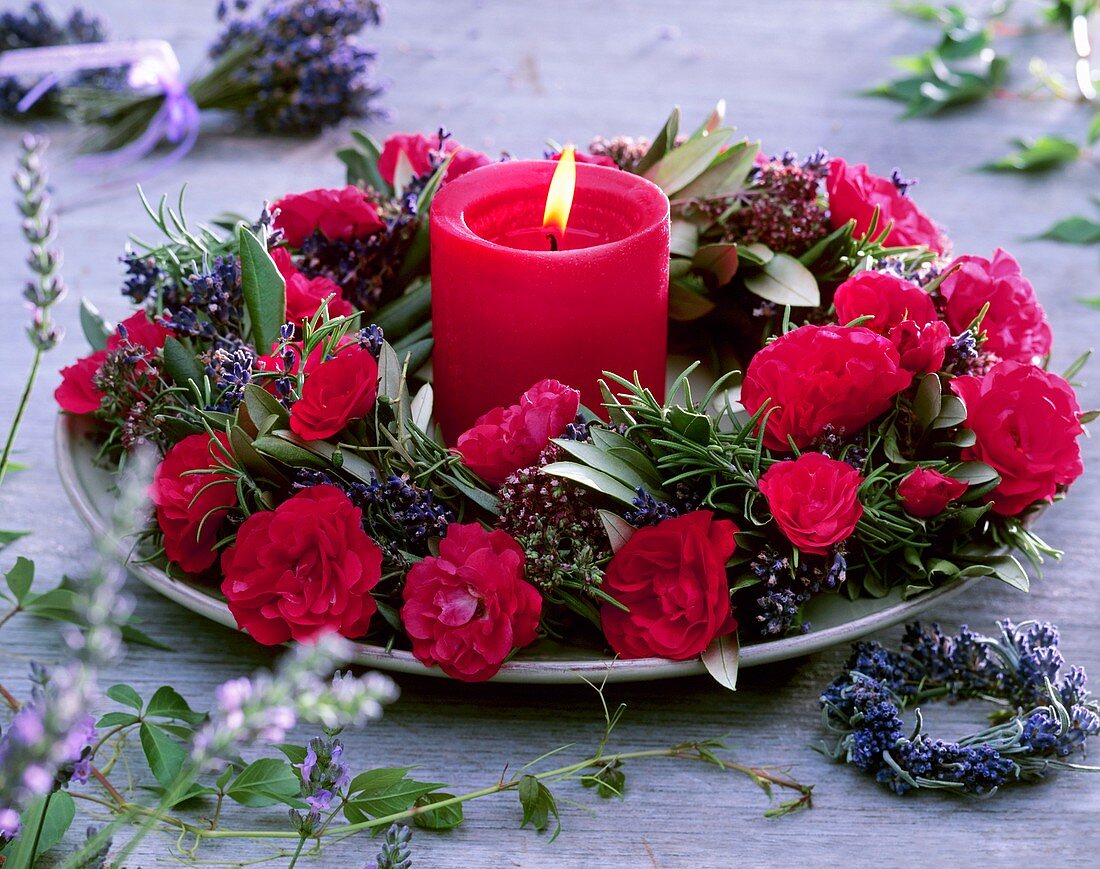 Wreath of red roses and herbs around red candle