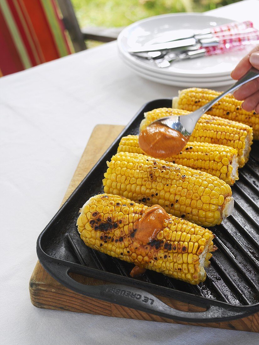 Spreading paprika butter on grilled corn on the cob