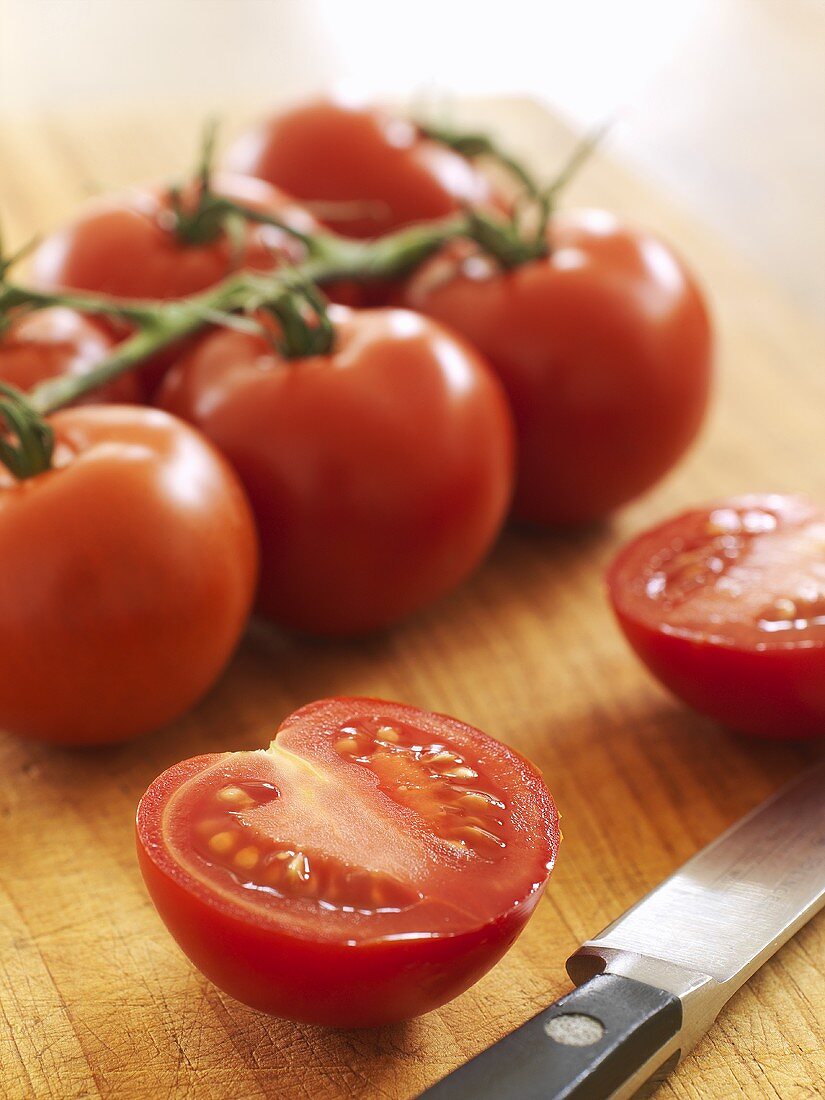 Halved tomato with knife and tomatoes on the vine