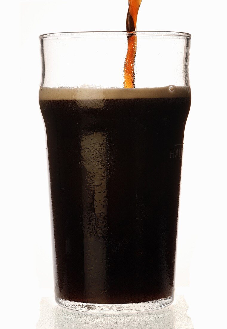 Ein Glas dunkles Bier einschenken (Sorte Stout, England)