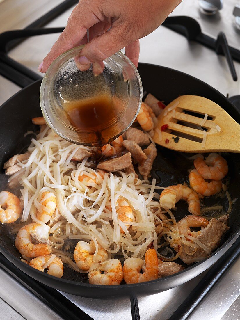 Adding fish sauce to a pan of shrimps and glass noodles