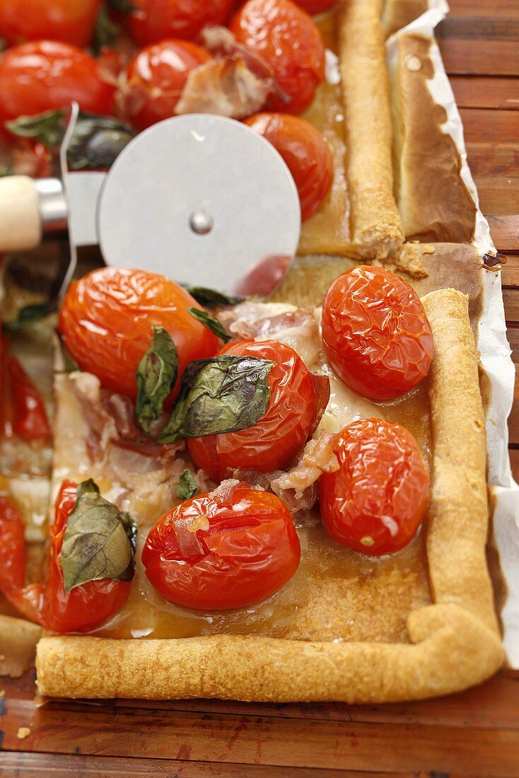 Pizza topped with ham and cocktail tomatoes, pizza cutter