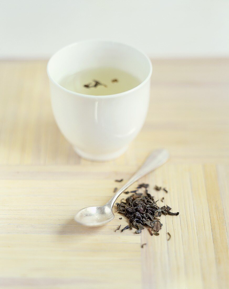 Ein Schälchen grüner Tee und Teeblätter