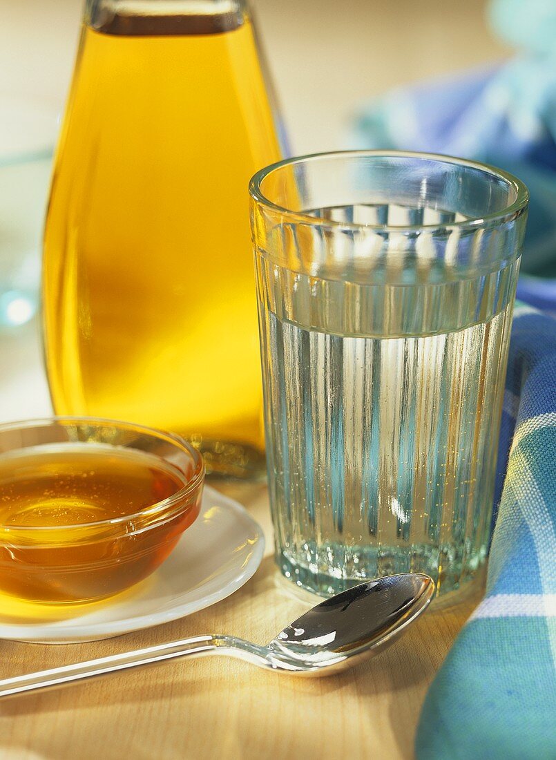 Glass of water, dish of honey and bottle of cider vinegar