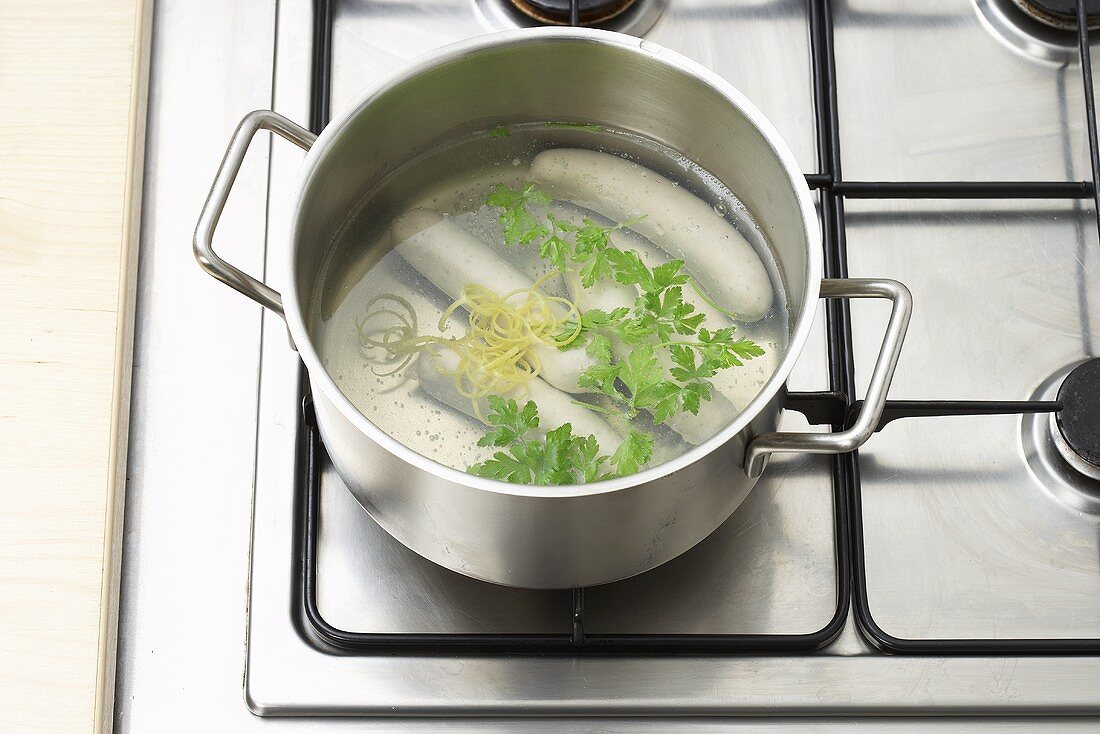 Boiling white sausages (Weisswurst) with lemon peel and parsley