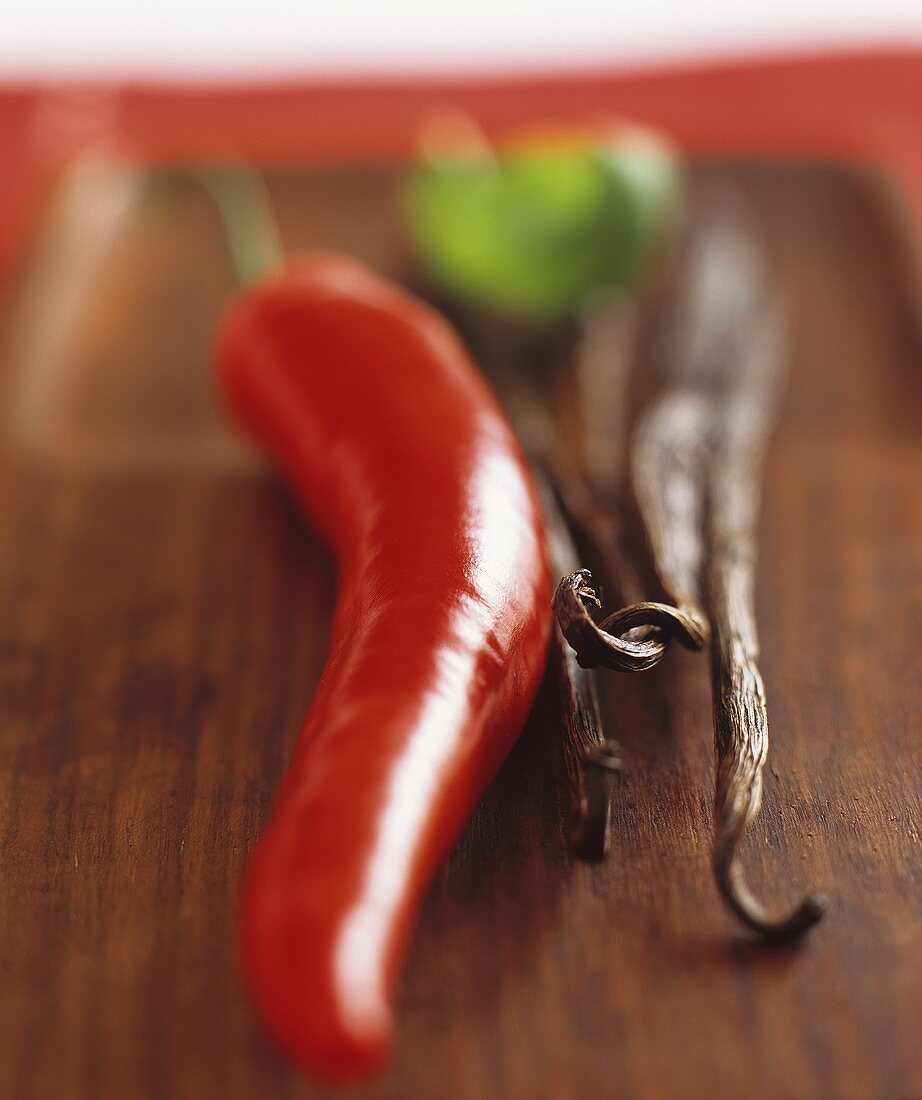 Vanilla pods and a red chilli pepper on a wooden board