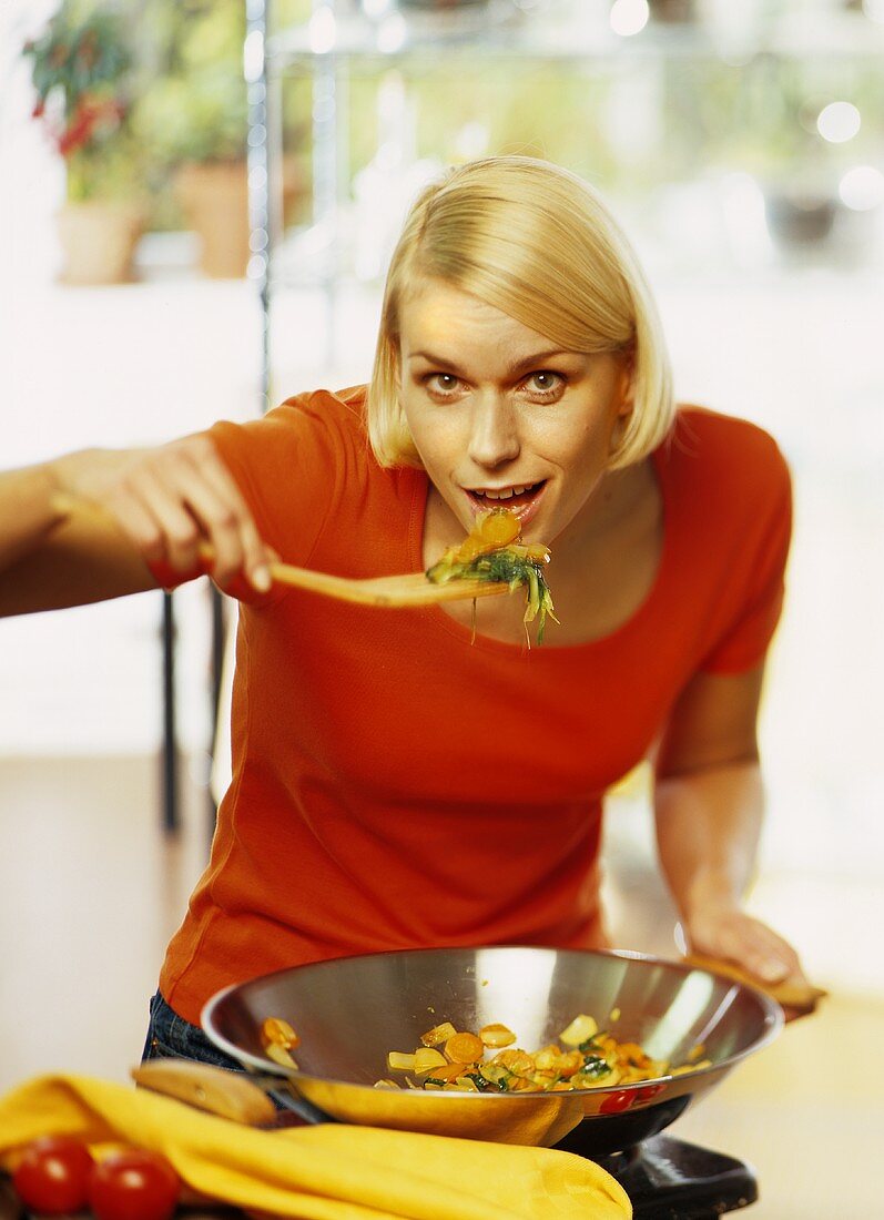 A young woman tasting food from a wok