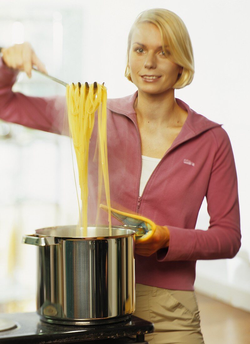 A young woman taking spaghetti out of a pot of water