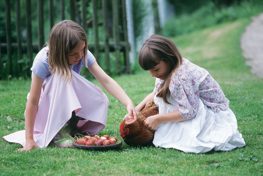 Zwei Mädchen mit Ostereiern und einem Huhn im Gras