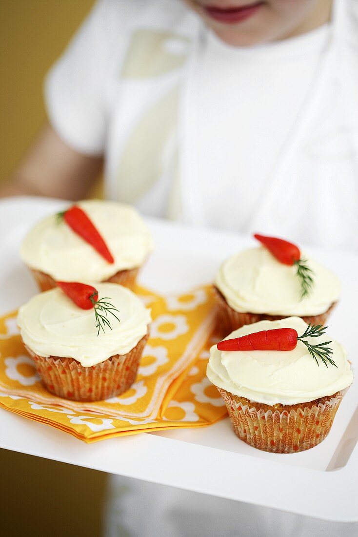 A child holding a tray of carrot cupcakes