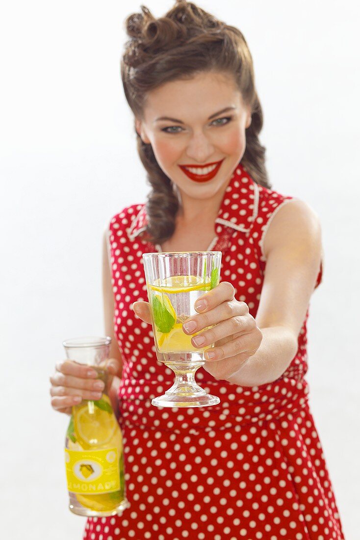 Mädchen im Retro-Look bietet ein Glas Zitronenlimonade an