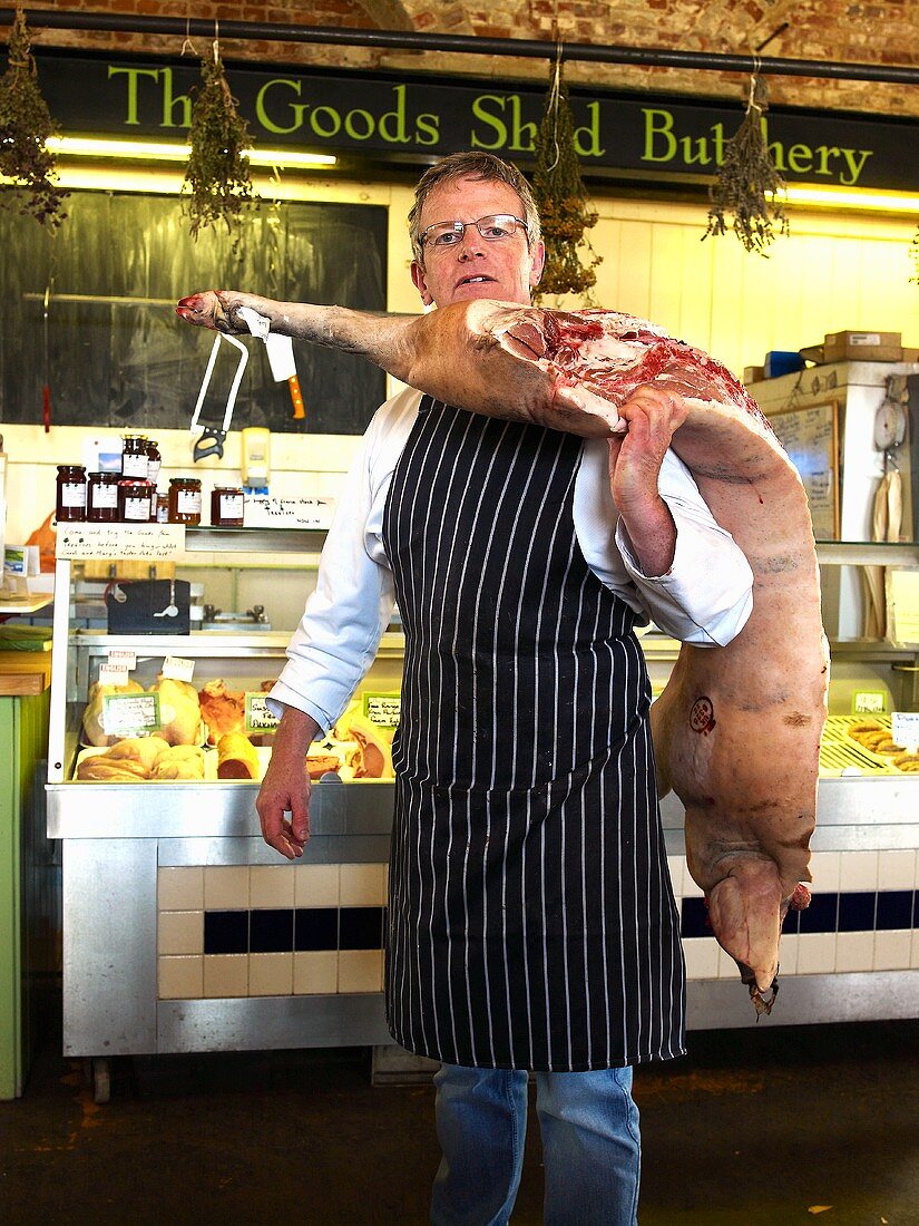 Metzger hält eine Schweinehälfte auf einem Bauernmarkt in England