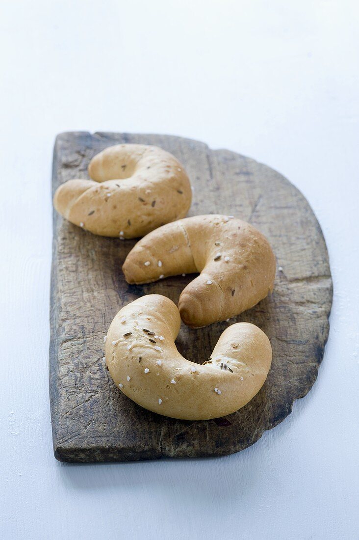 Three cresent-shaped rolls with salt and caraway on a wooden board