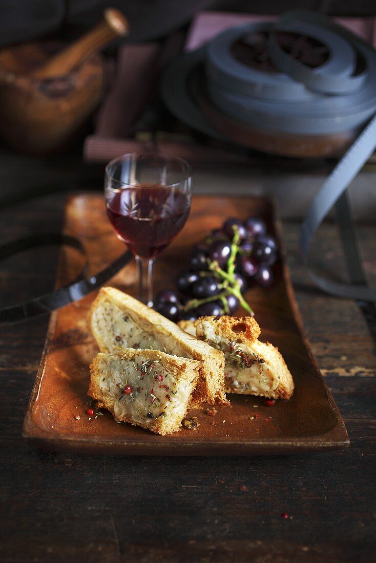 Röstbrot mit Käse, Rosmarin und Paprika, dazu Rotwein und Weintrauben