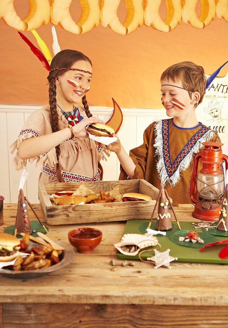 Zwei Kinder als Indianer verkleidet essen Hamburger auf Faschingsparty