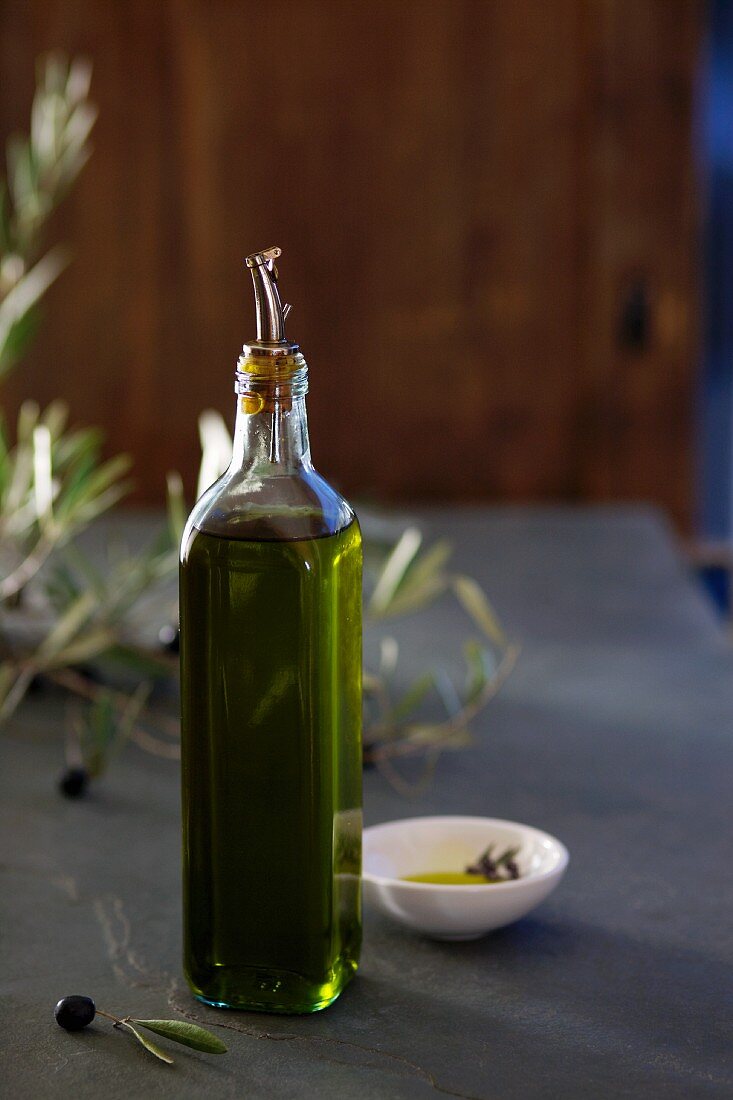 A bottle of olive oil, black olives and a olive sprig
