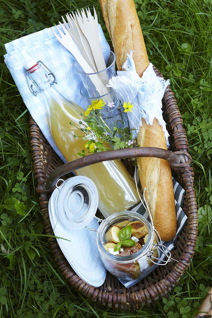 A picnic basket filled with juice, baguette and potato salad