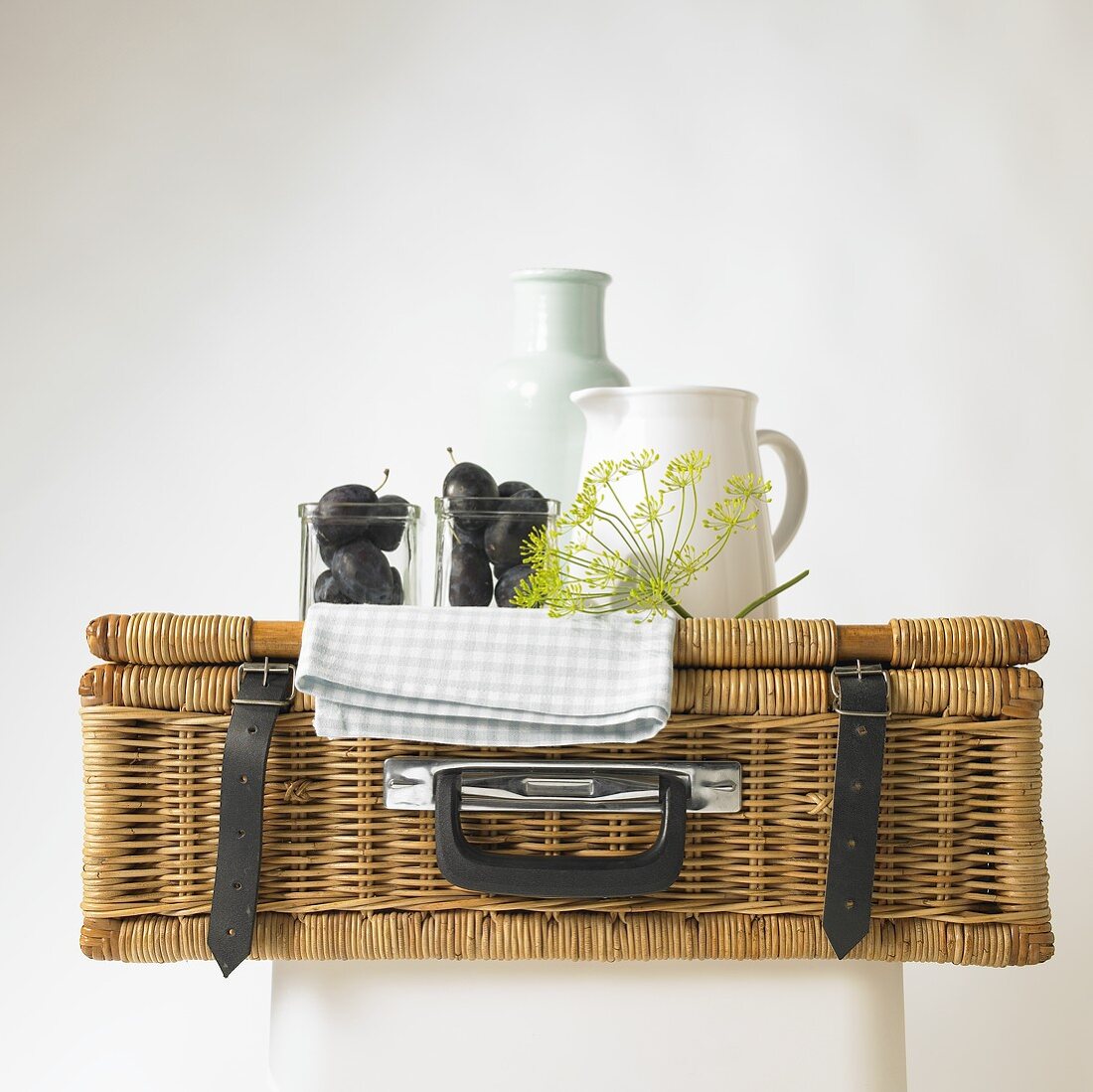A picnic basket with plums, dill flowers and a porcelain jug