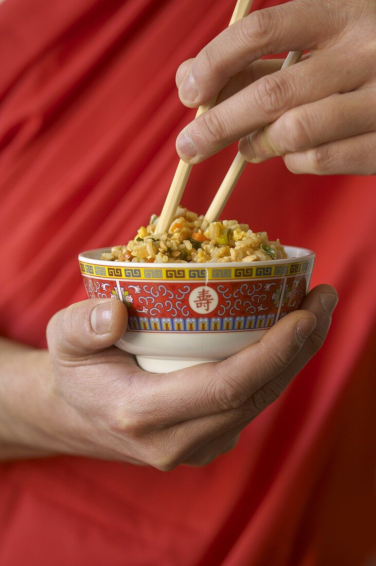 Hand hält Schale mit asiatischem Reisgericht