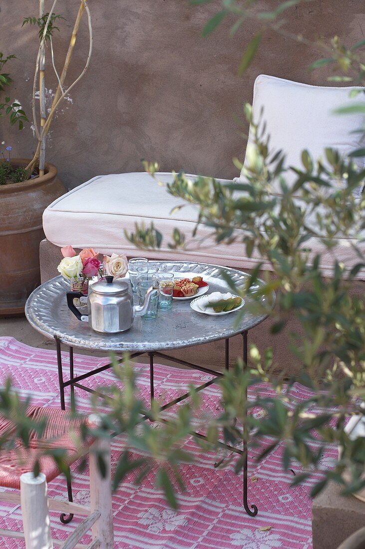 A Moroccan living room with a pot of tea, glasses and sweets on a table