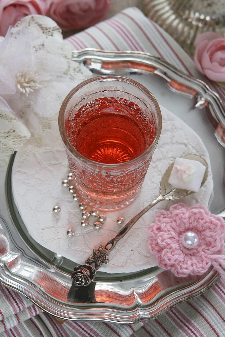 Ein Glas Hagebuttentee, Silberperlen und Häkelblume
