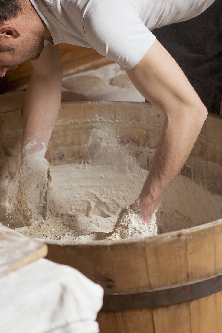 Baker kneading dough in a wooden tub