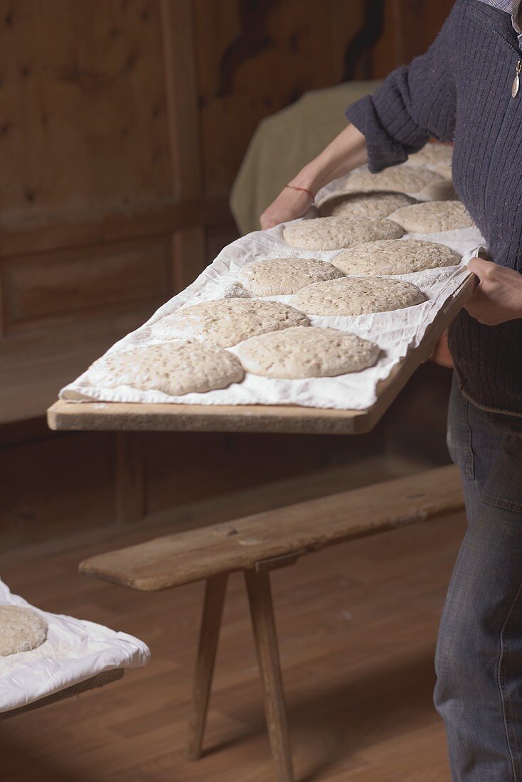 Frau trägt Holzplatte mit ungebackenen Broten