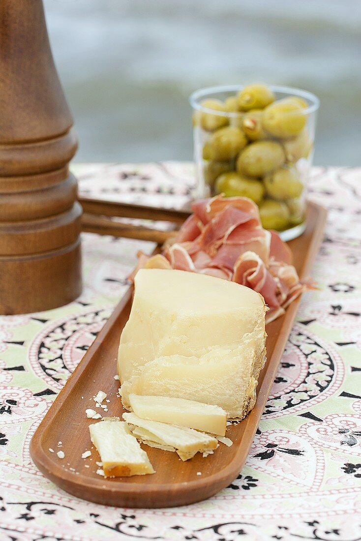Käse, Rohschinken und Oliven auf einer Holzplatte