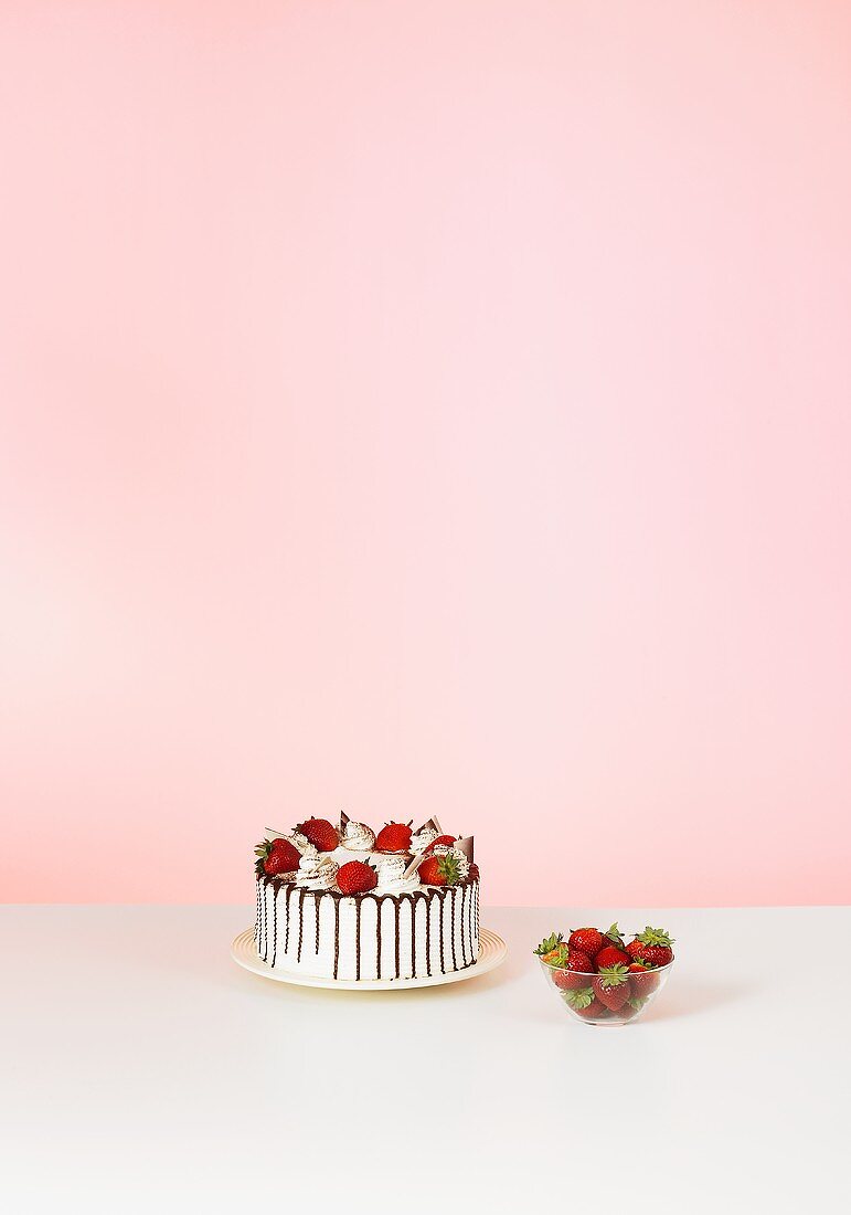 Kuchen mit Erdbeeren dekoriert und Schälchen mit Erdbeeren