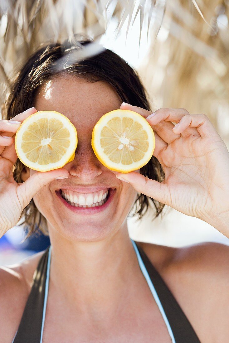 Junge Frau hält zwei Zitronenhälften vor die Augen