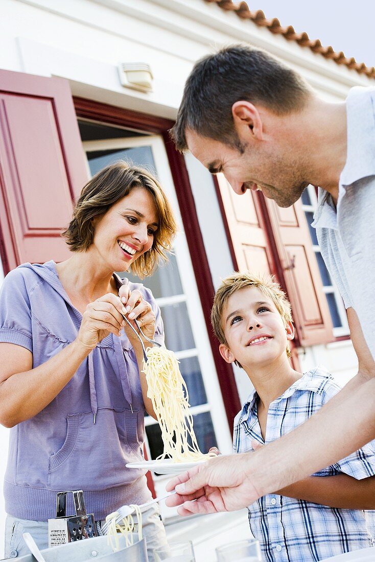 Familie mit Sohn isst Spaghetti im Freien