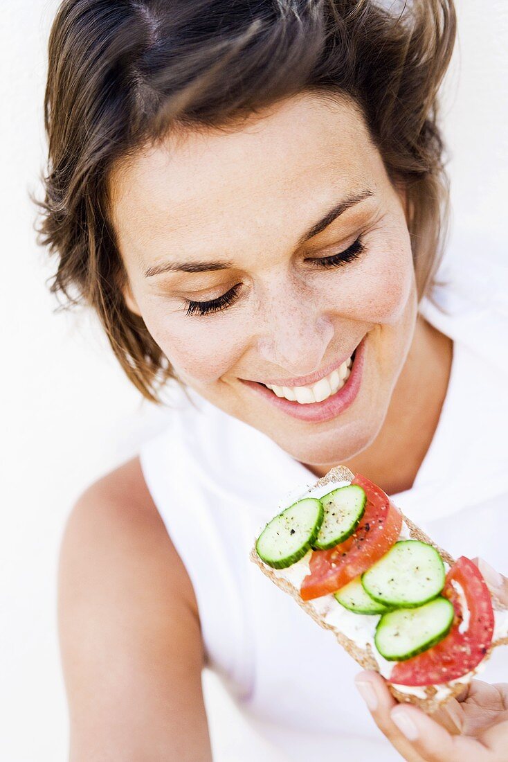 Young woman eating crispbread with soft cheese and salad