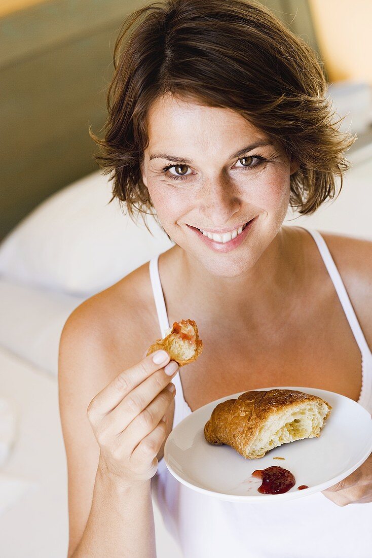 Junge Frau isst Croissant mit Marmelade