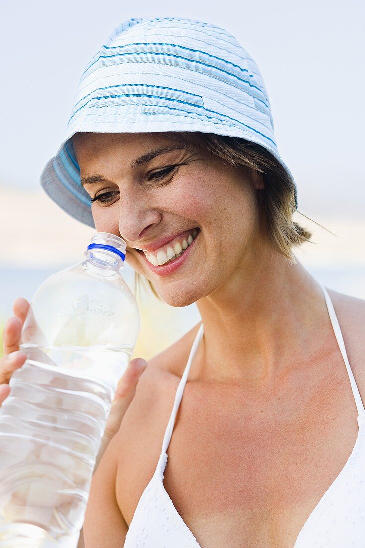 Frau mit Sommerhut trinkt Mineralwasser