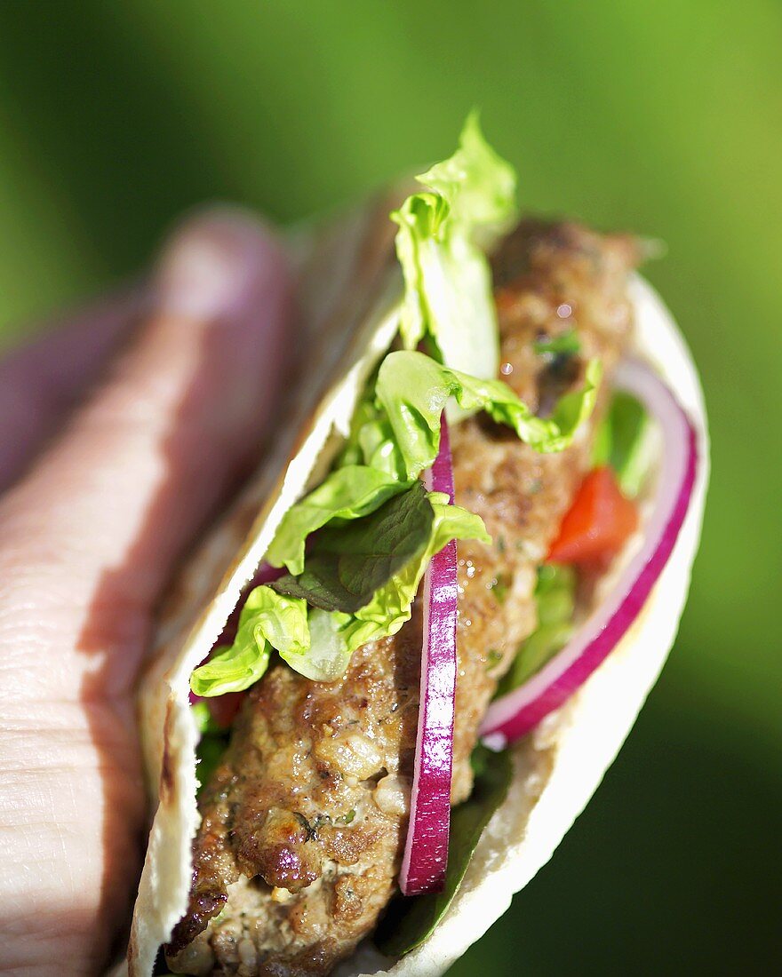 Hand holding pita bread filled with lamb burger and salad