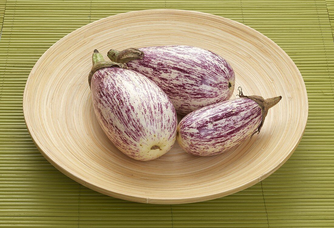 Three purple and white aubergines on plate
