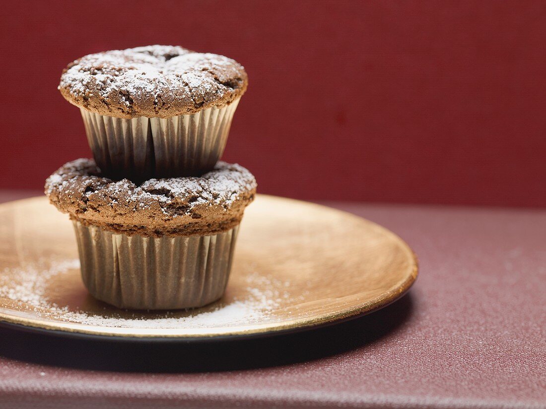 Two chocolate muffins dusted with icing sugar, stacked