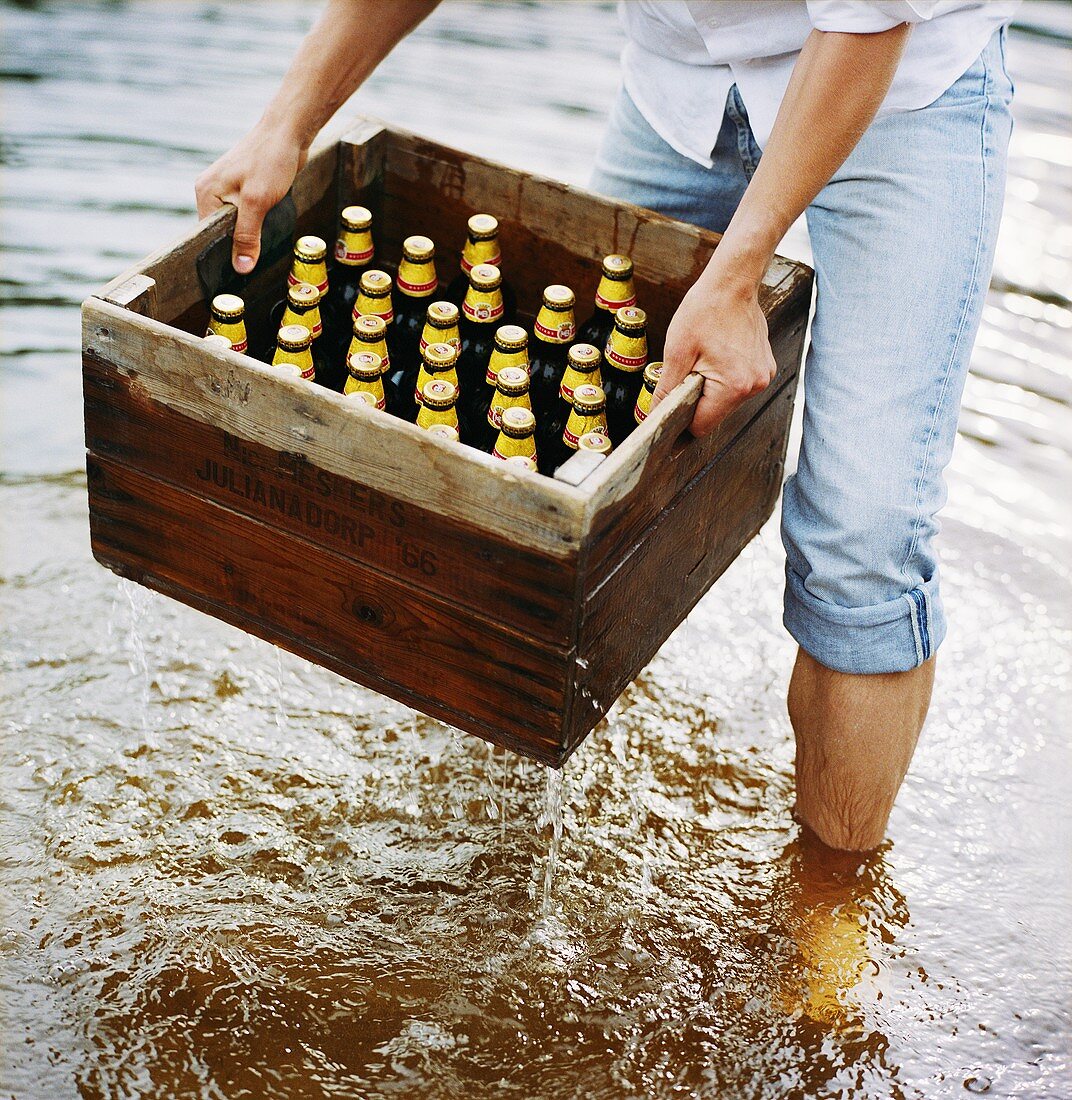 Mann hebt einen Kasten Bier aus dem Wasser