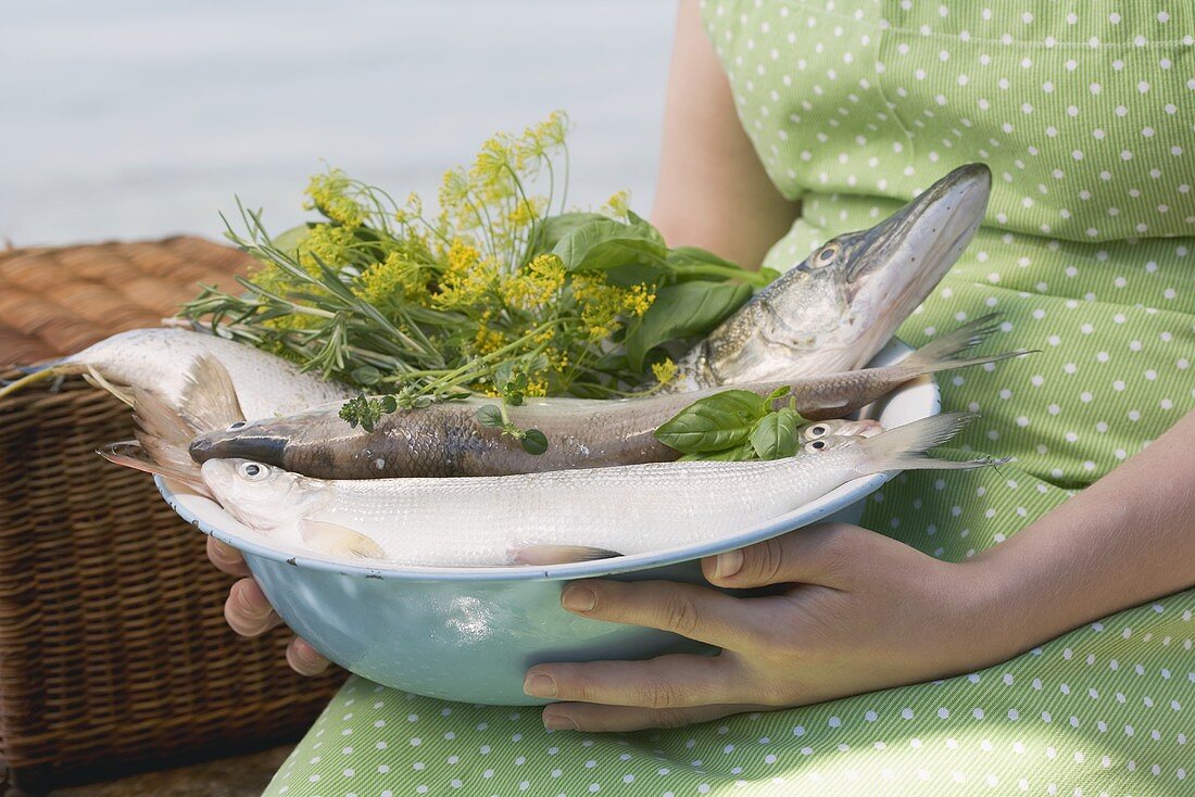 Woman holding bowl of freshly caught fish and herbs