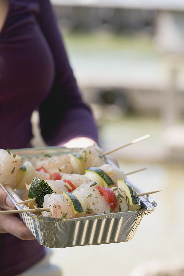 Frau hält Aluschale mit Fisch-Gemüse-Spiessen zum Grillen