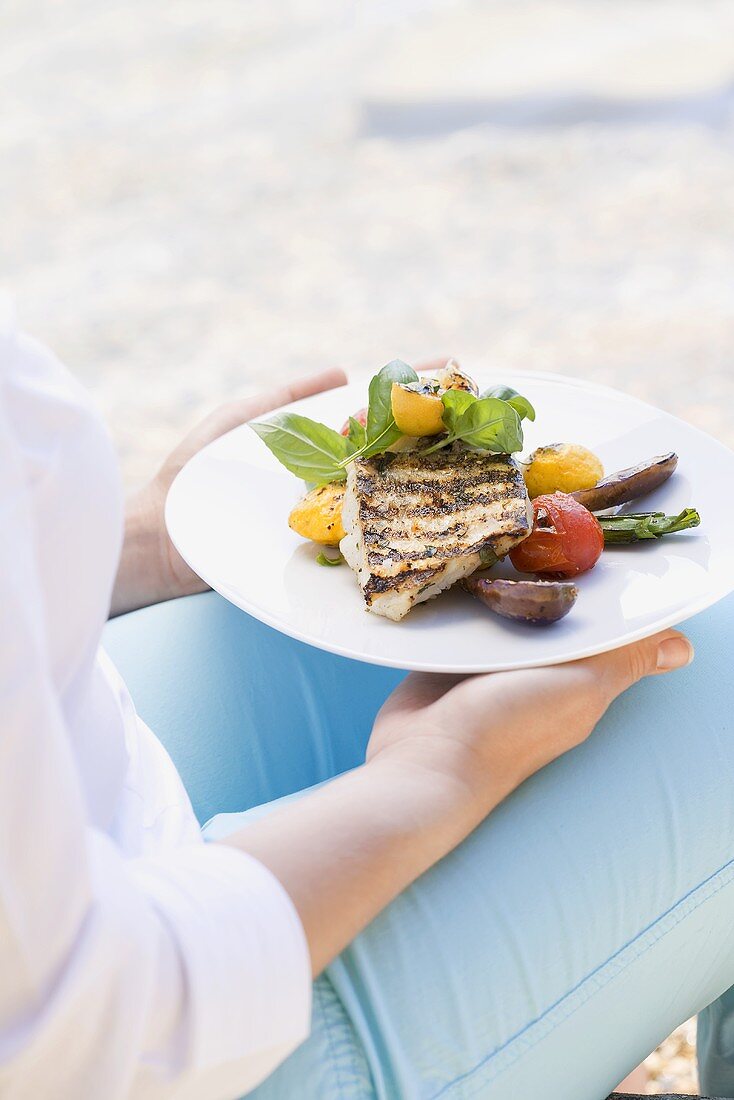 Frau hält Grillteller (Fischfilet mit Gemüse) im Freien