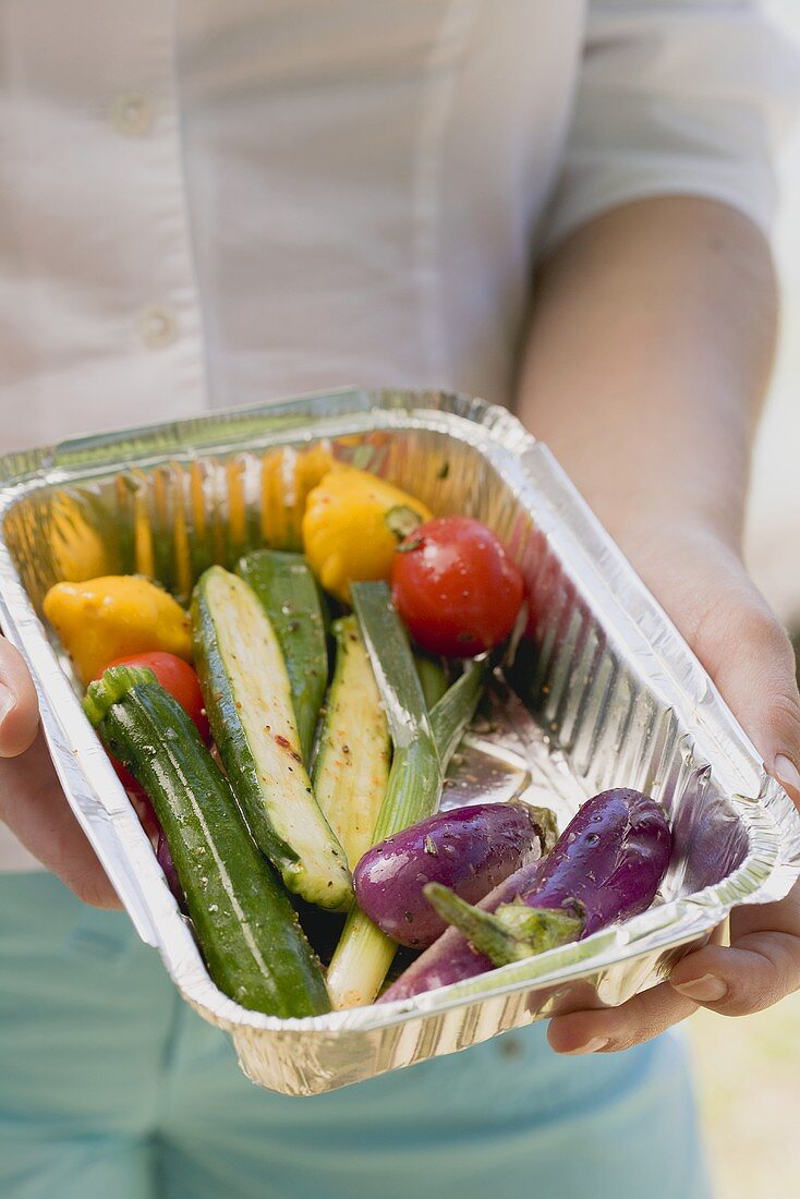Woman holding barbecued vegetables in aluminium dish