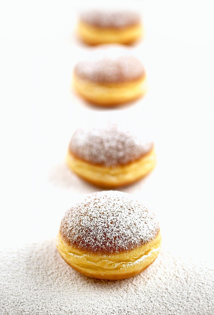 Four doughnuts sprinkled with icing sugar in a row