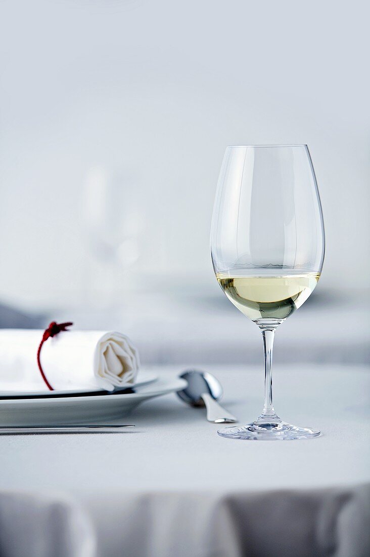 Glass of white wine on table laid in white
