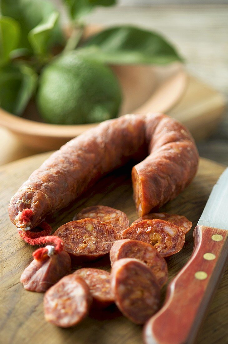 Partly sliced chorizo on chopping board with knife