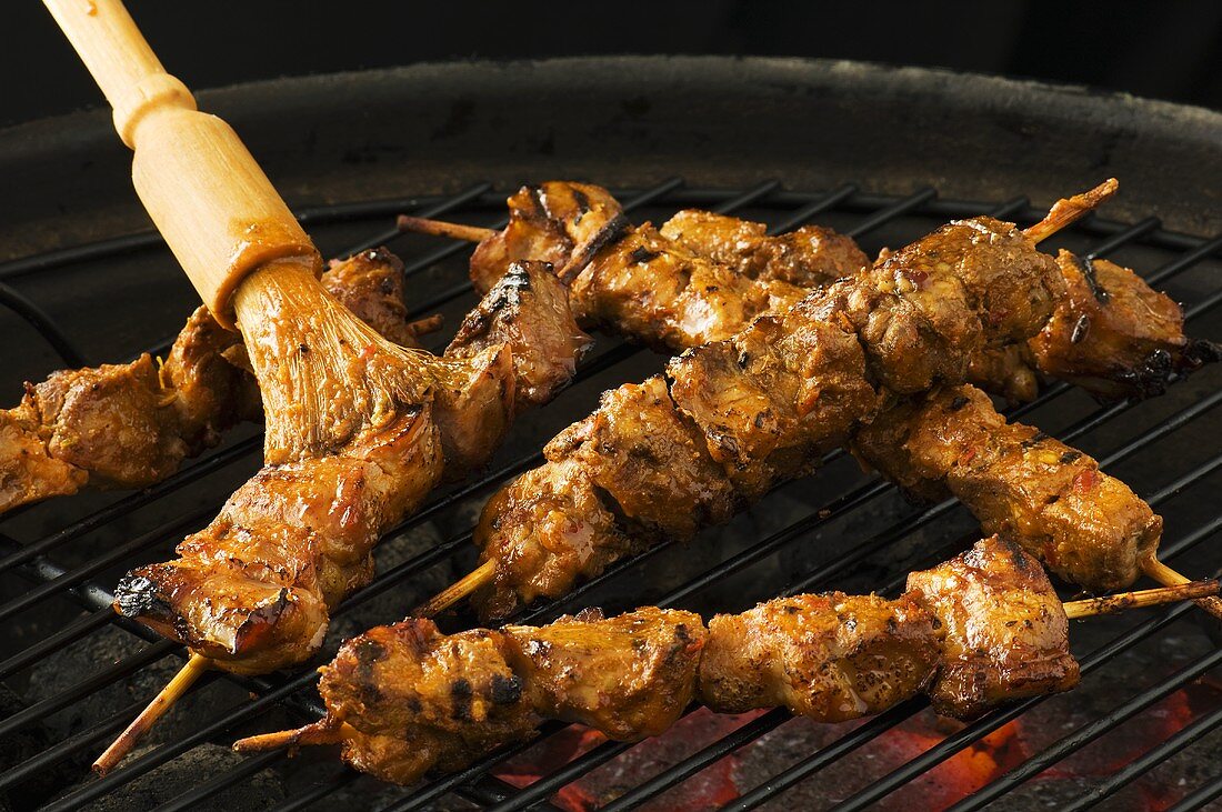 Brushing pork kebabs on barbecue with marinade