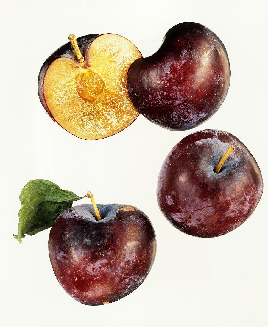 Two whole plums and one halved plum against white background