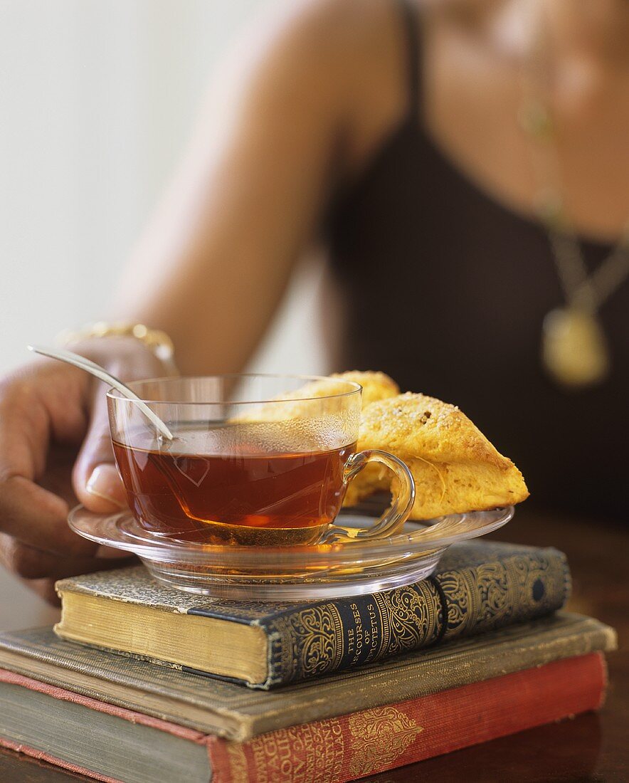 Frau stellt Tasse mit Tee & Scones auf Bücherstapel