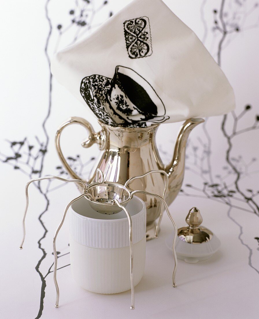 Silver teapot, tea strainer, tea beaker and printed napkin
